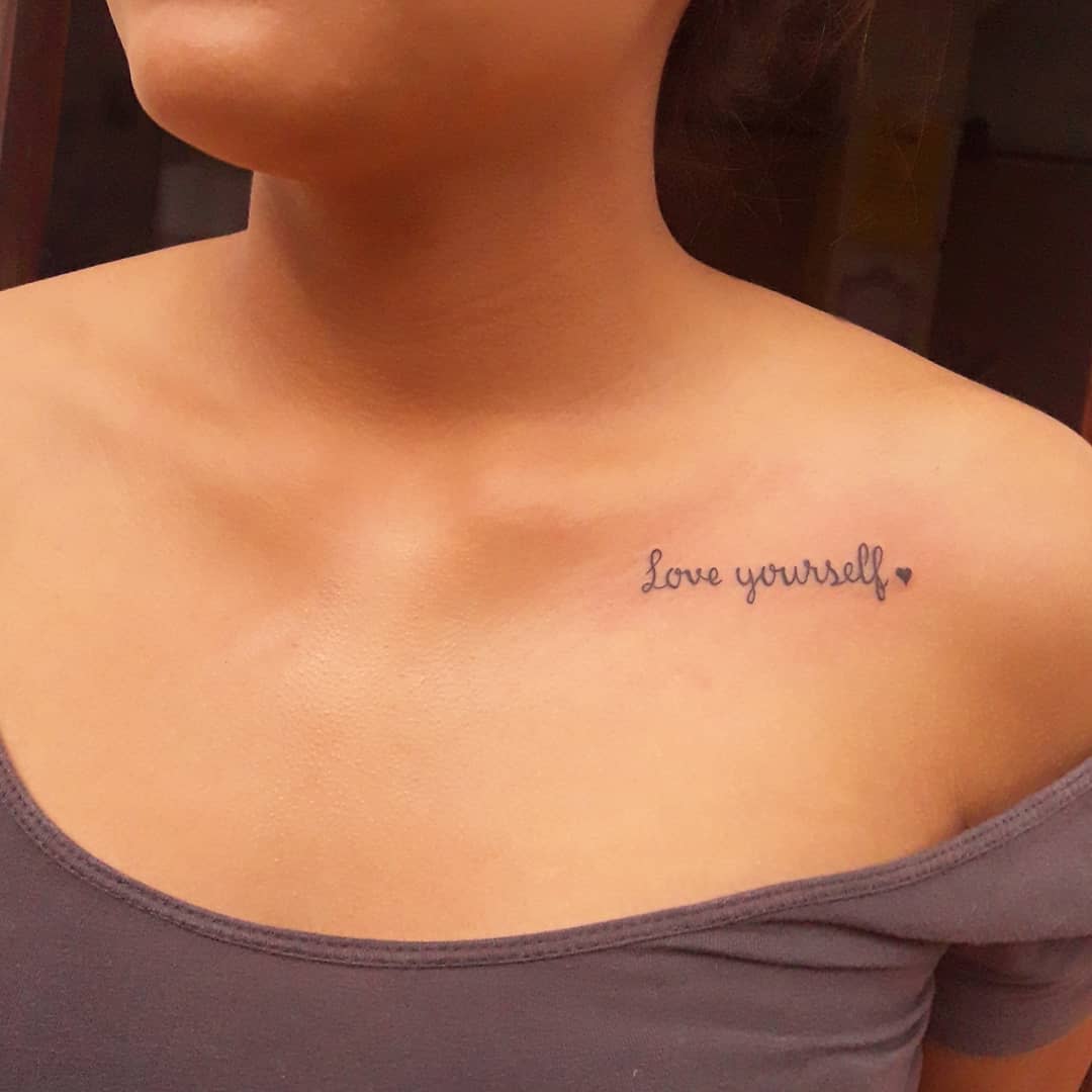 Love yourself" chest tattoo on someone wearing an off-shoulder top